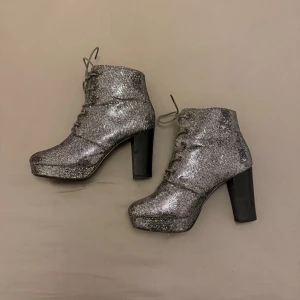 Glittriga silver boots med klack - Snygga boots i glittrigt silver med hög klack och snörning. Perfekta för att ge en extra touch till din outfit. De har en robust klack och en bekväm passform. Ena skorna är det lite skavt på (se bild) inget som syns när man har dom på. 