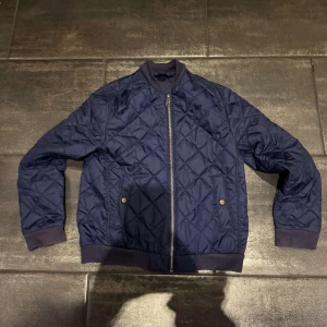Blå quiltad jacka från Polo Ralph Lauren - Säljer en snygg blå quiltad jacka från Polo Ralph Lauren. Jackan har en dragkedja framtill och ribbade muddar vid ärmslut och nederkant. Den är för barn så ganska liten
