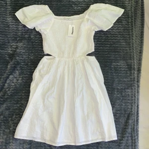 Vit klänning från Kappahl - Helt oanvänd ny Charmig vit klänning med prislapp från Kappahl med korta puffärmar och en smockad överdel. Klänningen har en luftig kjol och är perfekt för varma dagar. Den är tillverkad i ett lätt och bekvämt material. Passar även bra med ett par tights under till kallare dagar vid festliga tillfällen✨💄