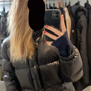 Jättesnygg glansig jacka från raph lauren, nästan aldrig använd  - Säljer en svart dunjacka med huva. Jackan har en pufferdesign med knappar och dragkedja framtill. Perfekt för kyliga dagar.