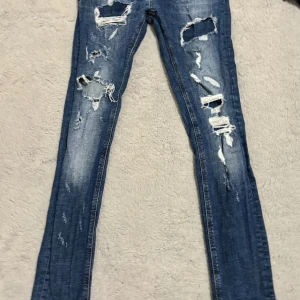 Blå Philipp Plein jeans med slitningar - Snygga blå jeans från Philipp Plein med coola slitningar och en super straight passform. Jeansen har en klassisk design med knappgylf och märkets logga på baksidan. Perfekta för en trendig look!