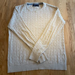 Beige stickad tröja från Jack & Jones - Säljer en stilren beige stickad tröja från Jack & Jones. Tröjan har ett klassiskt flätmönster och långa ärmar med ribbade muddar. Perfekt för kyligare dagar.