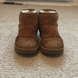 Bruna boots från UGG - Säljer ett par bruna boots från UGG med mjukt foder inuti. Är ganska slitna pga saltfläckar. Perfekta för kyliga dagar med sin varma och bekväma design. De har en klassisk look med rund tå och är tillverkade i mocka. Storlek 38. Köptes för 2000