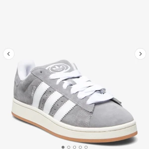 Gråa Adidas Campus sneakers - Snygga gråa Adidas Campus sneakers i mocka med vita detaljer och klassiska tre ränder. Skorna har en bekväm passform och vit sula med gummidetaljer. Perfekta för en stilren vardagslook. Passar båda 38/39. Använda 1 gång