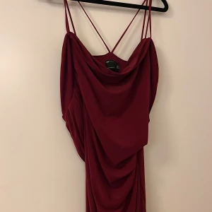 Vinröd långklänning med drapering - Elegant vinröd långklänning med tunna axelband och vacker drapering. Perfekt för festliga tillfällen med sin stilrena design och smickrande passform.