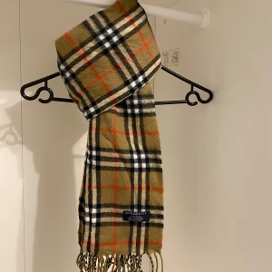 Burberry - Säljer nu denna Snygga halsduk från Burberry i beige. Tillverkad i 100% mjuk kashmir med fransar i ändarna. Perfekt för att hålla dig varm och stilren under kyliga dagar. Halsduken är i mycket fint skick. Hör av dig vid funderingar☺️