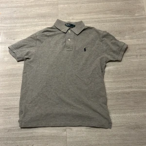 Grå pikétröja från Ralph Lauren - ⚜️Säljer en klassisk grå pikétröja från Ralph Lauren!!⚜️100% Äkta original pris 2200!! Tröjan har korta ärmar och knappar vid kragen. Perfekt för en stilren look. Skick 9/10. Med inga deflekter då den tyvärr inte kommit till användning. Snabb affär 299. Kontakta vid övrig information