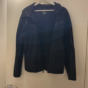 Svart jacka från Nike - Säljer en svart jacka från Nike med dragkedja och huva. Jackan har långa ärmar och en stilren design med Nike-logga på bröstet. Perfekt för en sportig look.