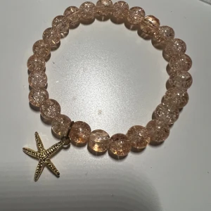 Armband med stjärndetalj - Snyggt armband med glittriga, genomskinliga pärlor och en guldig sjöstjärna som hänge. Perfekt för att ge en touch av havsinspiration till din stil.