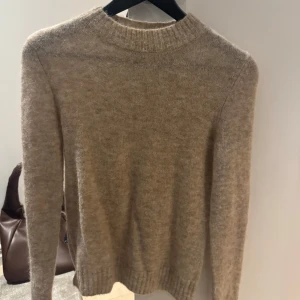 Beige tröja från Zara - Säljer en mysig beige tröja från Zara, tillverkad i en mjuk blandning av alpacka, ull och nylon. Perfekt för kyliga dagar med sin klassiska design och ribbade detaljer vid ärmslut och nederkant. Den är helt oanvänd