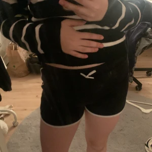 Svarta shorts med vita detaljer - Säljer ett par svarta shorts med vita kantdetaljer och snörning i midjan. Perfekta för en avslappnad stil.