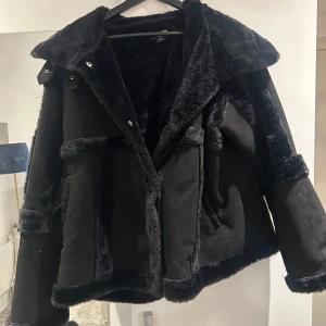 Svart pälsjacka - Snygg svart pälsjacka med mjukt foder och bred krage. Jackan har långa ärmar och stängs med knappar framtill. Perfekt för kyliga dagar när du vill hålla stilen. Normal i storleken. Nypris 700kr