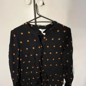 Säljer en svart blus med orange prickar från Object. Blusen har en enkel design med långa ärmar och en bekväm passform. Perfekt för både vardag och festliga tillfällen. 🖤🧡