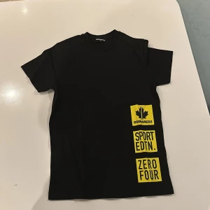 Svart t-shirt från Dsquared2 - Snygg svart t-shirt från Dsquared2 med coola gula tryck på framsidan. Perfekt för sportiga tillfällen eller en casual look. T-shirten är kortärmad och gjord i ett bekvämt material.