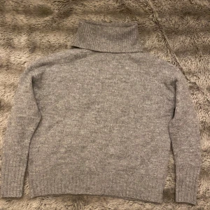 Grå stickad polotröja - Mysig grå stickad polotröja perfekt för kyliga dagar. Den har en hög polokrage och långa ärmar med ribbade muddar. Tröjan är i mycket bra skick och passar perfekt för både höst och vinter. En klassisk och stilren design som funkar till det mesta!