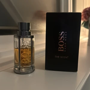 Hugo Boss The Scent - Säljer en elegant och maskulin parfym från Hugo Boss, The Scent. Flaskan är stilren med en metallisk ram och genomskinligt glas som visar den gyllene doften inuti. Perfekt för kvällar och speciella tillfällen. Kommer i originalförpackning.