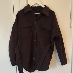 Vinröd/brun jacka från Gina Tricot - Säljer en snygg brun jacka från Gina Tricot i storlek S. Den har långa ärmar och knappar framtill, samt praktiska fickor på bröstet. Perfekt för höst och vår! 🧥