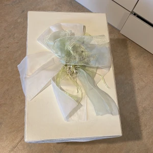 Vit presentask med grön rosett - En elegant vit presentask dekorerad med en stor grön rosett. . Asken har en stilren design  och är i bra skick, trots några mindre skavanker på kanterna och den är fortfarande stabil och håller bra . Höjd 30 längd 40 ,djupt 14,05 Djupt 18 och inte 14,05