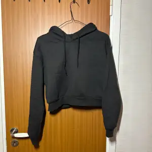 Svart croppad hoodie i mycket bra skick. Den har långa ärmar och en klassisk huva med dragsko. Perfekt för en avslappnad stil eller att mysa i hemma. Passar till alla säsonger!