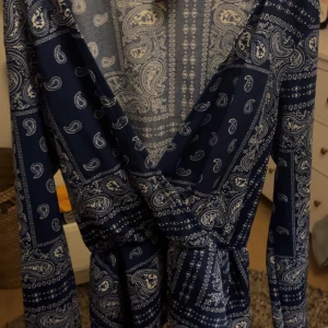 Mönstrad blus från Gina Tricot - Säljer en snygg mörkblå blus från Gina Tricot med paisleymönster i vitt. Blusen har långa ärmar och en omlott-design som ger en fin passform. Perfekt för både vardag och fest! Pris kan diskuteras.