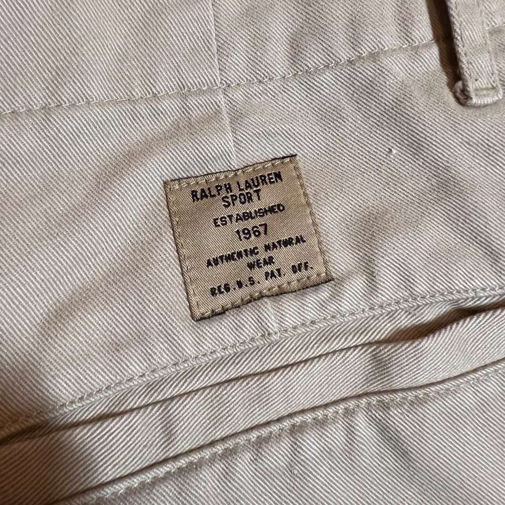 Säljer ett par snygga beige byxor från Ralph Lauren Sport i storlek M. Högmidjade.  De är tillverkade i 100% bomull vilket gör dem både bekväma och hållbara. Byxorna har en klassisk design med knapp och dragkedja framtill. Perfekta för både vardag, golf och lite finare tillfällen!. Jeans & Byxor.