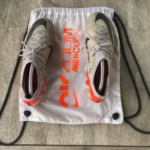 Säljer ett par Nike Air Zoom Mercurial fotbollsskor i mycket bra skick. Skorna är grå med svarta och röda detaljer, perfekt för fotbollsträning. De har snörning och en snygg design med Zoom-dämpning för extra komfort på planen.