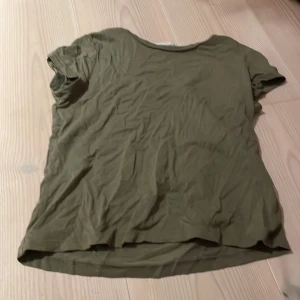 Olivgrön t-shirt från KappAhl - Säljer en olivgrön t-shirt från KappAhl i bra skick. Den är kortärmad och har en normal passform, perfekt för vardagsbruk. Materialet känns mjukt och bekvämt, vilket gör den idealisk för både sommar och vår. Passar bra till jeans eller shorts för en avslappnad look.