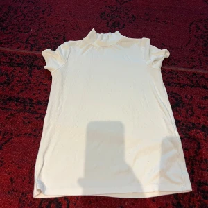 Vit ribbad polotopp - Säljer en stilren vit ribbad polotopp med korta ärmar. Perfekt för både vardag och festliga tillfällen. Toppen har en tight passform och är gjord i ett mjukt och bekvämt material. Passar bra till jeans eller kjol för en chic look.