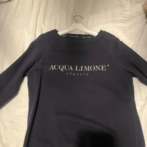 Mörkblå tröja från Acqua Limone - Säljer en snygg mörkblå tröja från Acqua Limone med deras klassiska logga på framsidan och en cool citrontryck på baksidan. Perfekt för en avslappnad stil. Tröjan har långa ärmar och är i bra skick. Passar perfekt till både jeans och joggers!