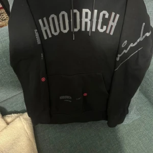 Svart hoodie från Hoodrich - Säljer en svart hoodie från Hoodrich i mycket bra skick. Den har en stor logga på bröstet och är gjord av en mjuk bomulls- och polyesterblandning. Perfekt för höst och vinter, med en skön passform och känguruficka framtill. Huvtröjan är både stilren och bekväm, idealisk för vardagsbruk. Pris kan diskuteras vid snabb affär 😁
