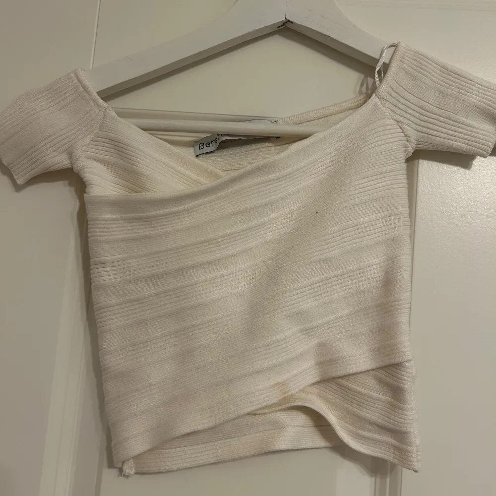 Säljer en superfin vit ribbad offshoulder topp från Bershka. Den har en snygg omlott-design och korta ärmar, perfekt för sommaren. Toppen är i bra skick och passar både till vardags och fest. Perfekt att matcha med ett par jeans eller en kjol! Bandage top aldrig använd dock en mini fläck framme!. Toppar.