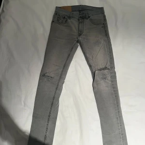Grå jeans Dondup  - Säljer ett par grå jeans med coola slitningar på knäna och bakfickan. De har en slim passform och är perfekta för en avslappnad stil. Jeansen har en klassisk femficksdesign och är i bra skick trots slitningarna. Perfekta för både vardag och fest!