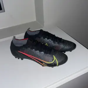 Säljer ett par svarta Nike fotbollsskor i mycket bra skick. De har en snygg design med gula och röda detaljer samt snörning. Perfekta för fotbollsträning eller match. Skorna är lätta och bekväma, vilket ger bra grepp på planen. Säljer dom också för att dom är för små för mig men dom är riktigt fina skriv vid minsta fråga eller fundering. 