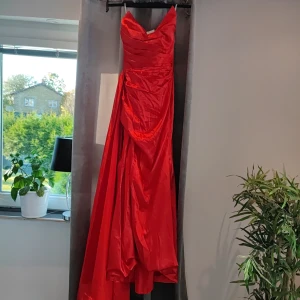 Röd bal  långklänning med snörning - Säljer en fantastisk röd långklänning i siden med en elegant snörning i ryggen. Klänningen har en vacker drapering och är perfekt för festliga tillfällen. Den är axelbandslös och har en smickrande passform. Perfekt för nyår eller en glamorös festkväll! ✨