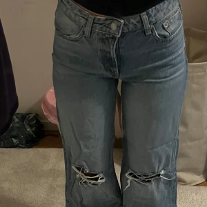 Blå jeans med slitningar - Säljer ett par blå jeans med coola slitningar på knäna. De har en klassisk femficksdesign och är perfekta för en avslappnad stil. Jeansen har en normal passform och är gjorda i ett slitstarkt denimtyg. Perfekta för både vardag och fest!