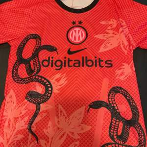 Säljer en cool röd fotbollströja från Nike med ett unikt ormmönster och blommor. Tröjan har korta ärmar och är perfekt för fotbollsfans. Den har Digitalbits-loggan på framsidan och är i mycket bra skick. Perfekt för att sticka ut på planen eller som en del av din samling! 🐍⚽ Tröjan är även helt ny med prislappar kvar och i storlek S