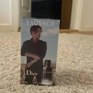 Säljer en flaska Sauvage Eau de Toilette från Dior, 100 ml. Flaskan är elegant med en mörk design och har en magnetisk kork med CD-loggan på toppen. Perfekt för den som vill ha en fräsch och maskulin doft. Kommer i originalförpackning