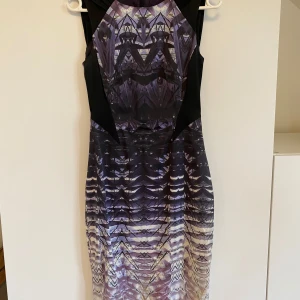 Mönstrad cocktail klänning från Karen Millen - Snygg klänning från Karen Millen med ett unikt mönster i lila och svart. Den har en figurnära passform och är ärmlös, perfekt för festliga tillfällen. Klänningen har en dragkedja i ryggen för enkel påklädning. Aldrig använd.