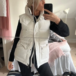 Vit dunväst med dragkedja - Säljer en snygg vit dunväst i mycket bra skick. Västen har en dragkedja och knappar framtill samt praktiska fickor. Perfekt för höst och vinter. 💞⭐️