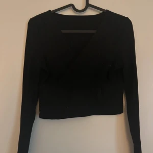 Svart topp  - Säljer en svart topp med lång ärm och v-ringad design. Perfekt för en stilren och enkel look. Toppen är tight och passar bra till både vardag och fest.
