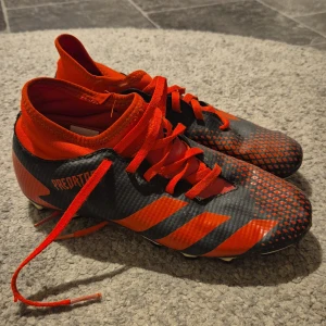 Adidas fotbollsskor i svart och rött - Säljer ett par Adidas fotbollsskor i mycket bra skick. De är svarta med röda detaljer och har snörning för perfekt passform. Skorna har en cool design med randigt och prickigt mönster, perfekt för fotbollsplanen. Storlek 37