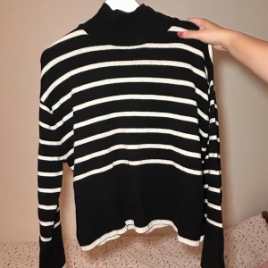 Svart och vit randig tröja - Säljer en snygg svart och vit randig tröja med polokrage. Perfekt för kyliga dagar med sin mysiga och stilrena design. Tröjan har långa ärmar och är i mycket bra skick. Skriv för fler bilder!