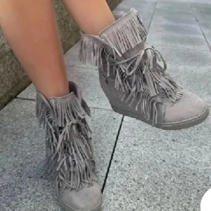 Grå boots med fransar - Snygga grå boots med massor av fransar. De har en bekväm kilklack och snörning framtill. Perfekta för höst och vår när du vill sticka ut lite extra. Materialet ser ut som mocka och de har en cool, avslappnad stil.