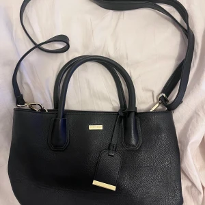 Svart handväska från Don Donna - Snygg och stilren svart handväska från DKNY i skinn. Väskan har både handtag och en justerbar axelrem för flexibel användning. Perfekt för både vardag och fest! 🖤