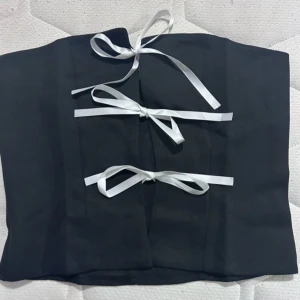 Svart korsett med vita band - Snygg svart korsett med vita knytband framtill. Perfekt för en festlig look eller att styla upp en outfit. Den har en elegant och stilren design som passar till många olika tillfällen.