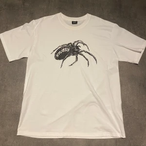 Stussy widow tee  - Säljer t-shirt från Stussy med ett stort svart spindeltryck på framsidan. T-shirten är i bomull och har en oversized passform. Perfekt för en avslappnad stil eller streetwear-look. 🕷️