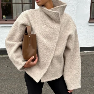 Beige teddyjacka - Säljer en supermysig beige teddyjacka. Perfekt för höst och vinter med sin varma och gosiga känsla. Jackan har en unik omlott-design och långa ärmar. Den är både stilren och bekväm, perfekt för kalla dagar. 🧥✨