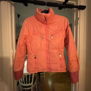 Moncler jacka  - Säljer en snygg rosa dunjacka från Moncler i bra skick. Jackan har långa ärmar och dragkedja framtill. Den är perfekt för höst och vinter med sin varma och mysiga design. Moncler-loggan syns på ärmen och en stor broderad detalj på ryggen. Passar perfekt för dig! Det är en ovanlig vintage i fint skick.