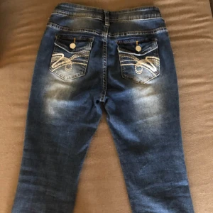 Blå jeans med broderade fickor - Säljer ett par snygga blå jeans i bra skick. De har en normal passform och är dekorerade med coola broderier på bakfickorna. Perfekta för både vardag och fest! 🕺