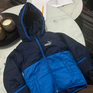 Blå och svart barnjacka från Puma  - Säljer en snygg blå och svart pufferjacka från Puma. Den är i mycket bra skick och redo för nya äventyr!